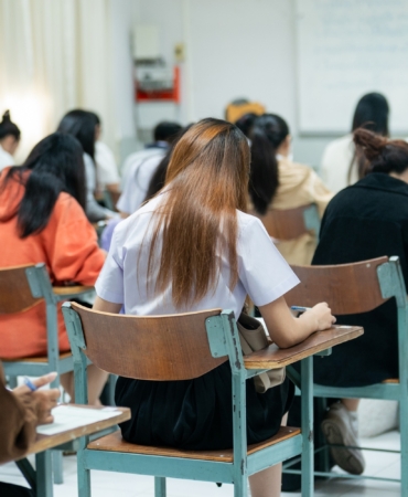Group,Of,Students,Sitting,In,Classroom,Desks,While,Writing,An